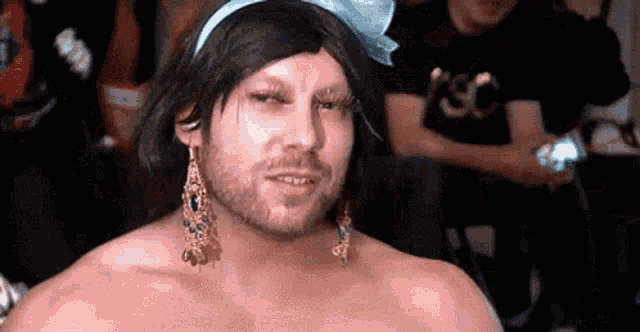 a man with a beard and earrings is wearing a wig and a bow .