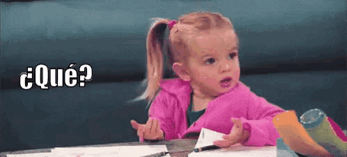 a little girl in a pink jacket is sitting at a table with a pen and a piece of paper .