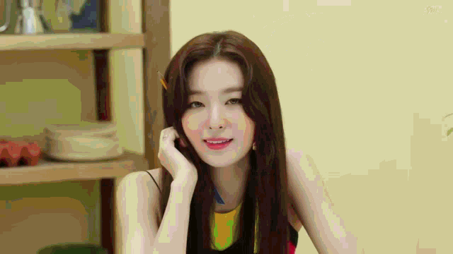 a woman with long hair is sitting in front of a wooden shelf and smiling .
