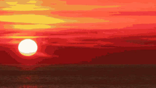 the sun is setting over the ocean in a red sky