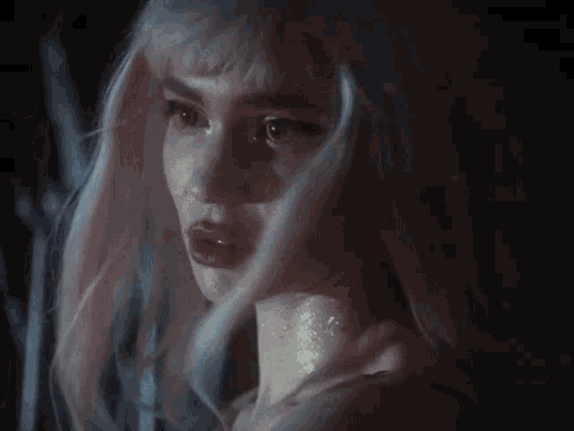 a woman with white hair and red lips looks at the camera