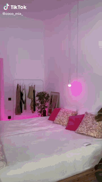 a woman in a red dress is standing in front of a bed in a bedroom with pink lights