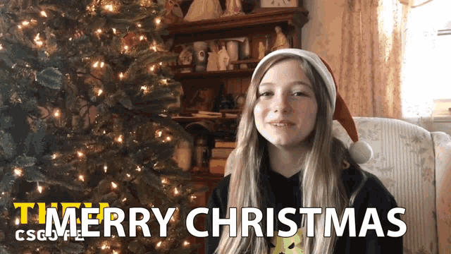 a girl in front of a christmas tree says merry christmas