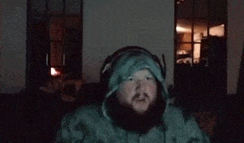 a man with a beard is wearing headphones and a hoodie and is dancing in a dark room .