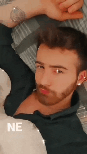 a man with a beard and a tattoo on his wrist is laying in bed .