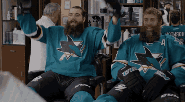 two men wearing sharks jerseys are sitting in a chair