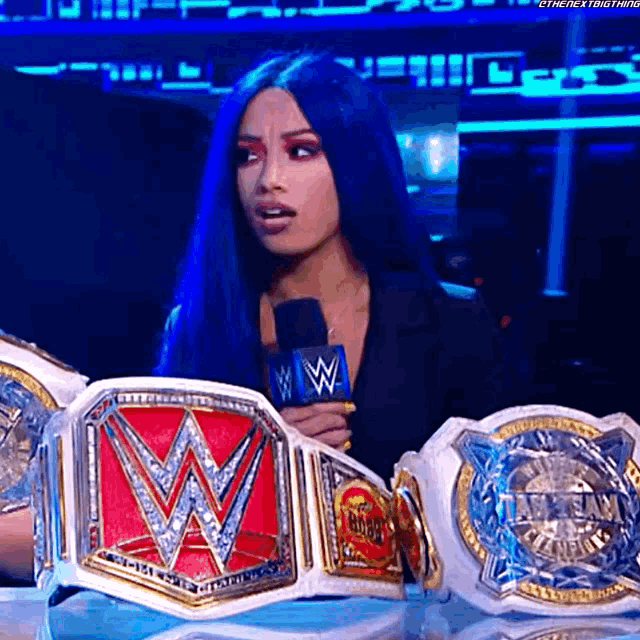 a woman with blue hair is holding a microphone while holding a wrestling belt .