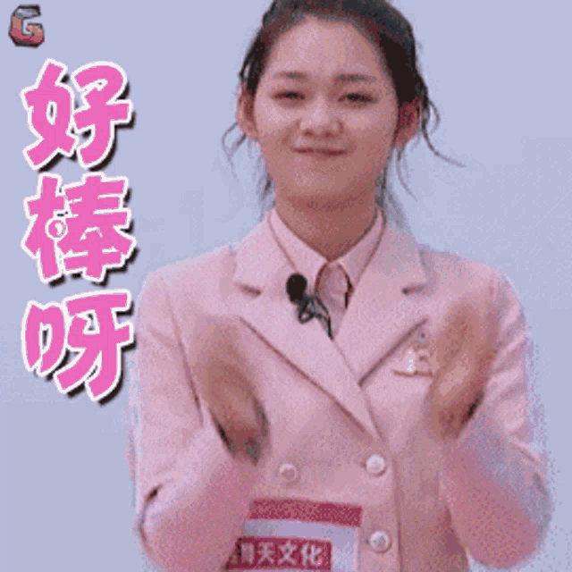 a woman in a pink suit is clapping her hands in front of a sign that says g