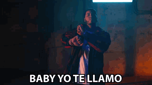 a man in a dark room with the words baby yo te llama written below him