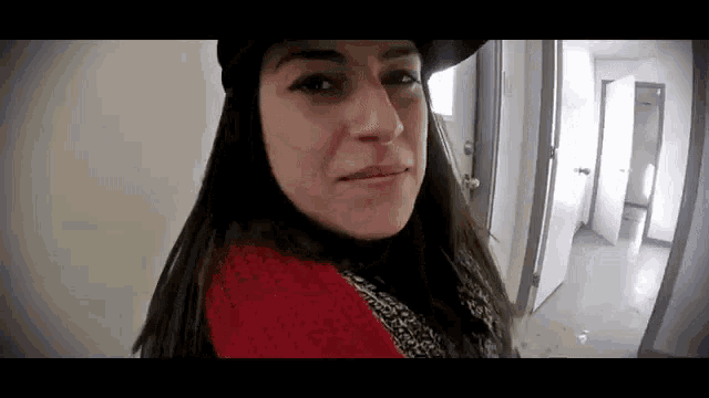 a woman in a red sweater and black hat is standing in a hallway .