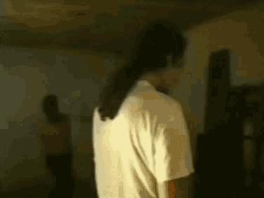 a man with long hair is standing in a dark room with a woman standing behind him .