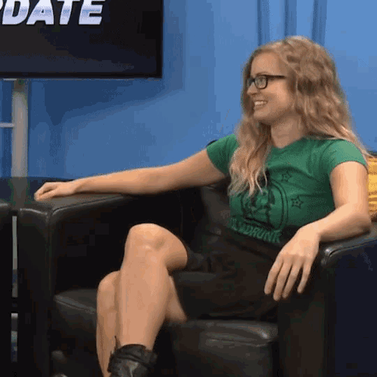 a woman wearing glasses and a green shirt with a skull on it sits in a chair