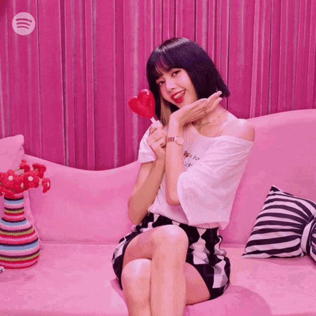 a woman sitting on a pink couch holding a lollipop