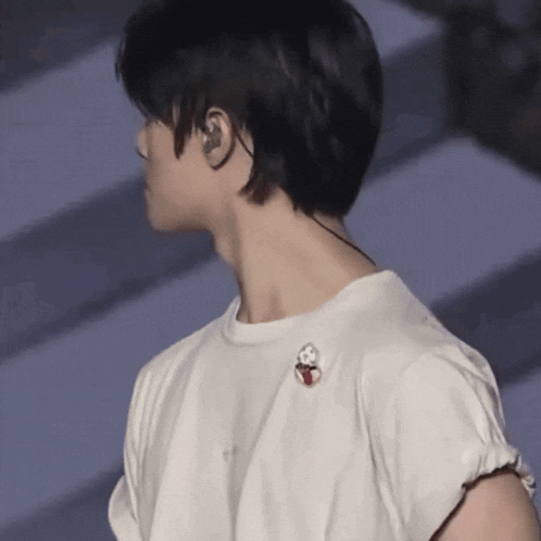 a man wearing ear buds and a white t-shirt has a pin on his shoulder