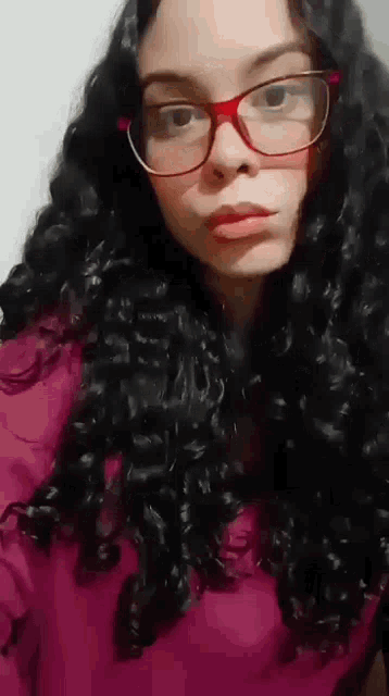 a woman with curly hair and glasses is wearing a purple shirt .