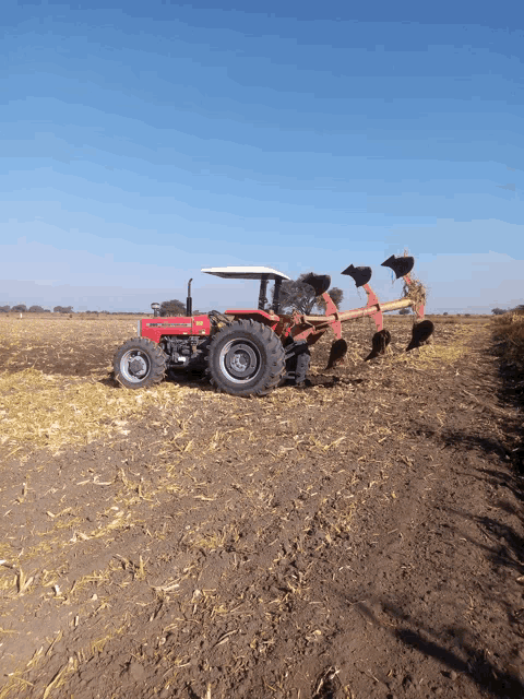 a red tractor is plowing a field with a plow attached