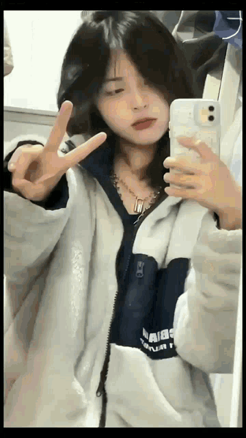 a girl is taking a picture of herself in the mirror and giving a peace sign