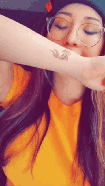 a woman with glasses and a tattoo on her wrist has her eyes closed