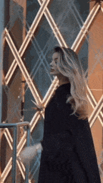 a woman in a black coat is standing in front of a building with a glass wall .