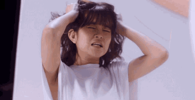 a woman in a white shirt is holding her hair and making a face .