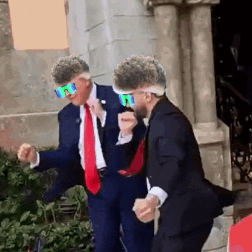 two men in suits and sunglasses are dancing together .