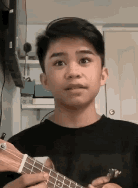 a young boy is playing a guitar and making a funny face .