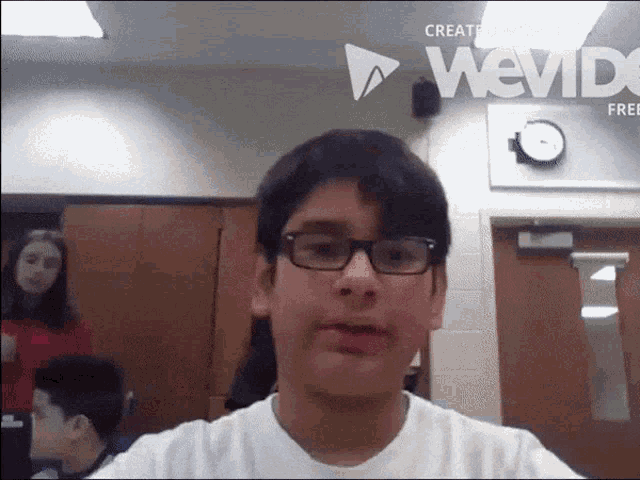 a boy wearing glasses is standing in front of a clock that says wevid on it