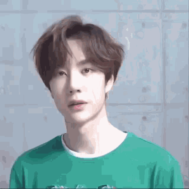 a young man wearing a green t-shirt is making a funny face with his eyes closed .