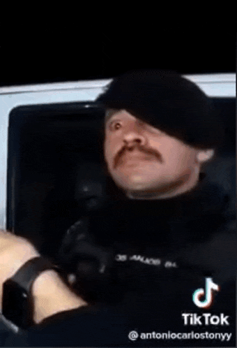a man with a mustache is wearing a black hat and gloves while sitting in a car .