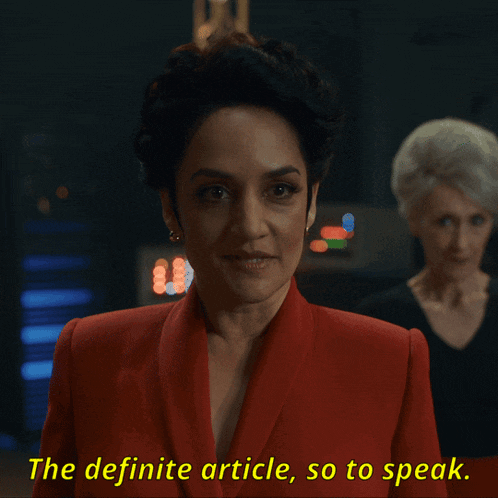 a woman in a red jacket is talking about the definite article so to speak