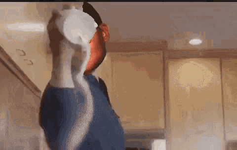 a man in a blue shirt is standing in a kitchen holding a bottle of milk .