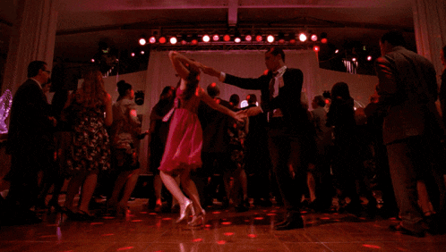 a woman in a pink dress is dancing with a man in a suit on a dance floor