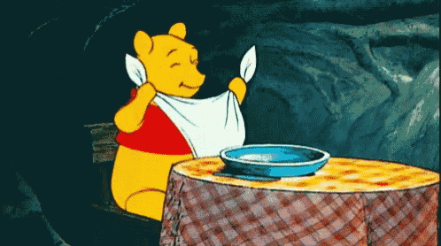 winnie the pooh is sitting at a table with a napkin around his neck