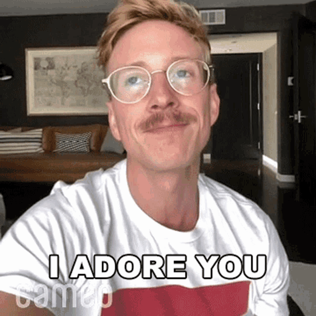 a man with glasses and a mustache is wearing a white shirt that says " i adore you "