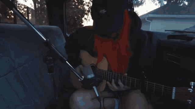 a woman with red hair is playing a guitar in a car with a microphone