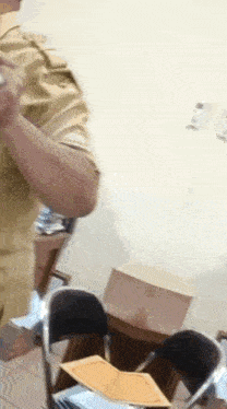 a man in a tan uniform is standing in a room holding a bottle of water