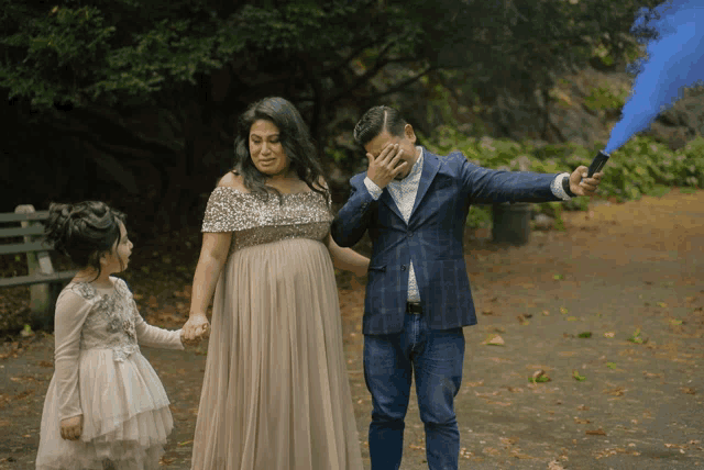 a man is covering his face while holding a blue smoke bomb while standing next to a pregnant woman and a little girl