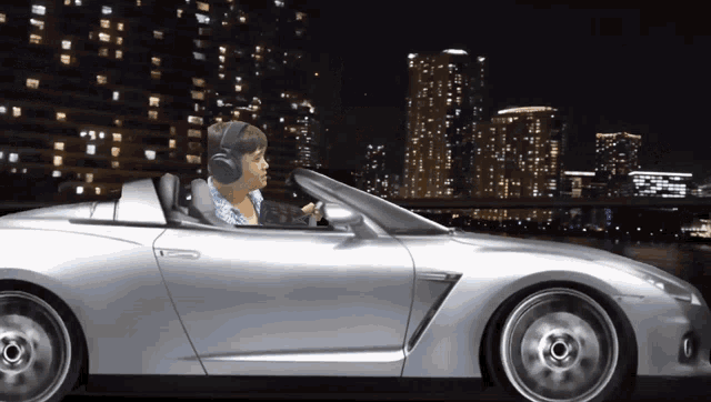 a man wearing headphones is driving a silver sports car at night