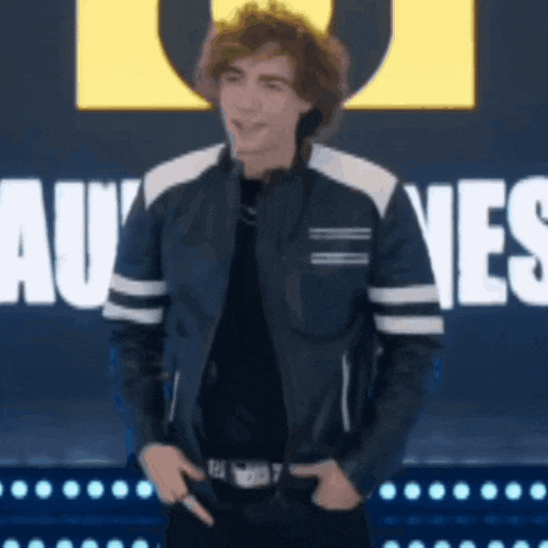 a young man in a leather jacket is standing in front of a sign that says " au "