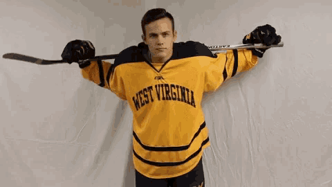 a man in a west virginia jersey is holding a hockey stick over his shoulder