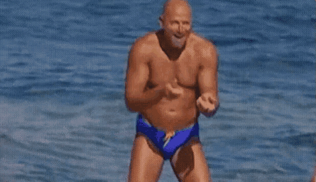 a shirtless man in blue swim trunks is jumping into the ocean .