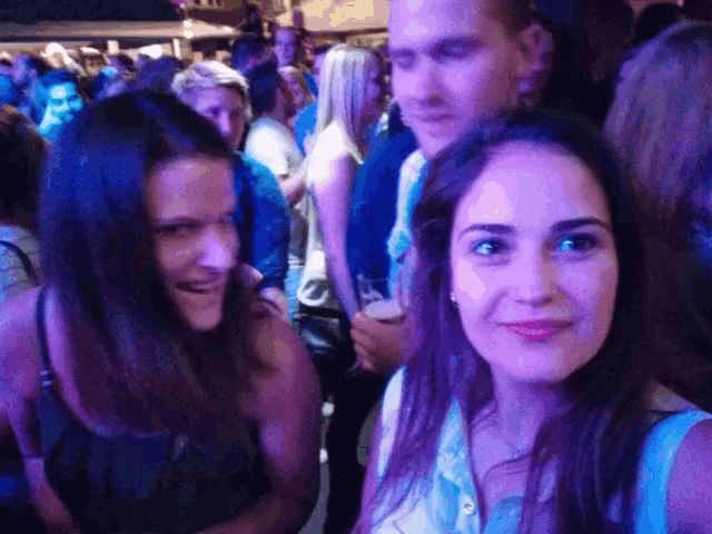 two women are posing for a picture in a crowd at a party