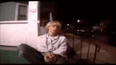 a man in a white shirt is sitting on the ground in front of a building at night .