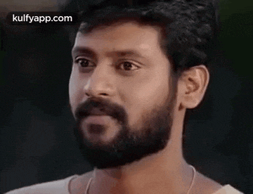 a man with a beard and a white shirt is looking at the camera .