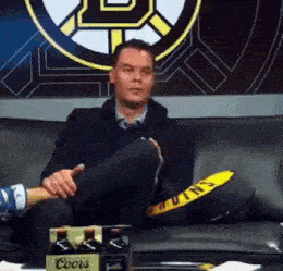 a man is sitting on a couch with his legs crossed in front of a coors sign .