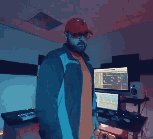 a man wearing a red hat and sunglasses is standing in front of a computer monitor