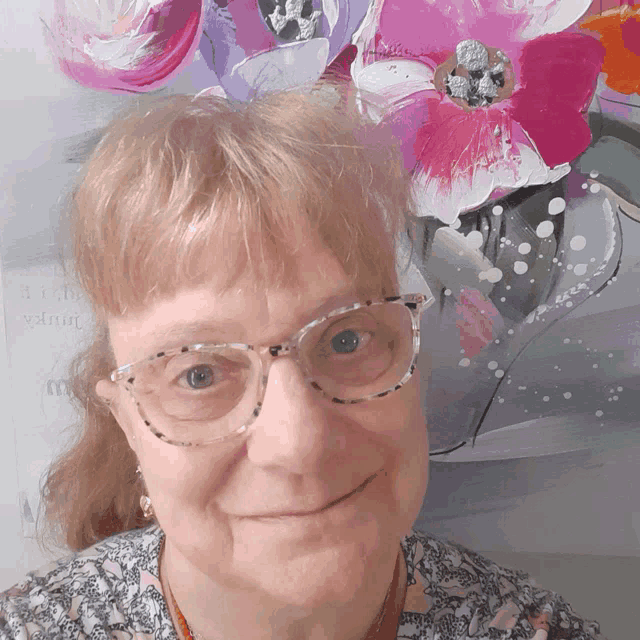 a woman wearing glasses is smiling in front of a painting