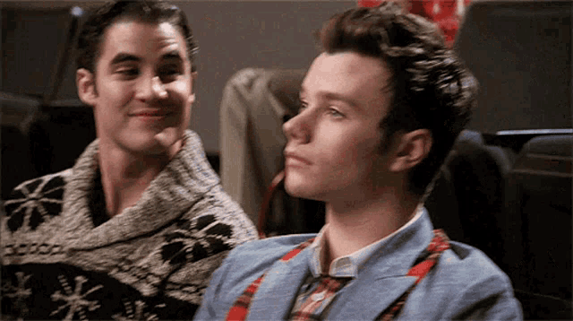 two men are sitting next to each other and one is wearing a sweater with snowflakes