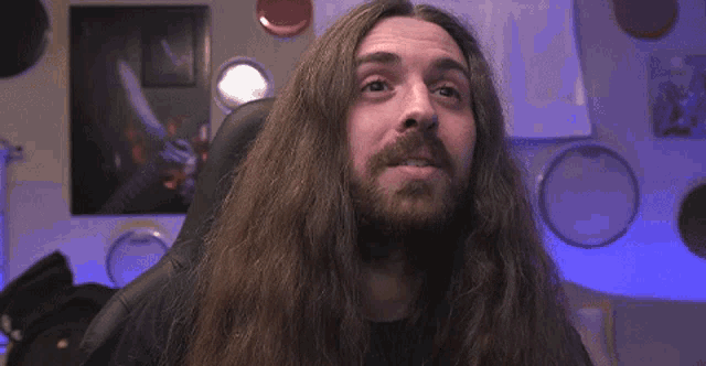 a man with long hair and a beard is sitting in a chair .