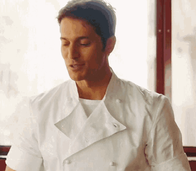 a man wearing a white chef 's coat is standing in front of a window with his eyes closed